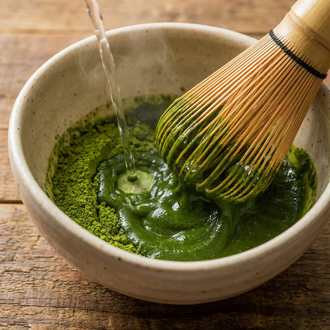 Añadiendo agua caliente al té matcha en un cuenco con chasen.
